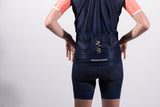 Close view of storage pockets on back of women's navy cycling wind vest. Deep pockets and gold reflective logo.