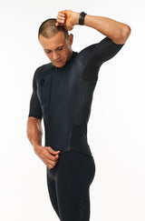Model lifting left arm of men's Hex Racer Jersey. Flexible black cycling jersey with mesh panels.
