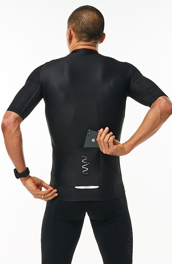 Model placing a phone in the back pockets of men's Onyx Hex Racer Jersey. Black cycling jersey with reflective pockets.