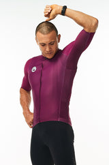 Model lifting left arm of men's Hex Racer Jersey. Flexible purple cycling jersey with mesh panels.