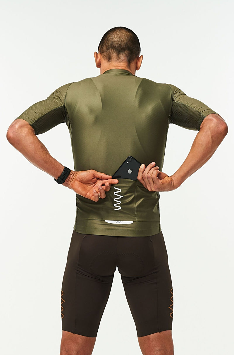 Model placing a phone in the back pockets of men's Olive Hex Racer Jersey. Green cycling jersey with reflective pockets.