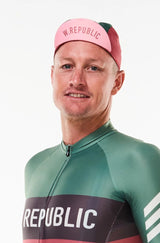 Model wearing WYN republic Alliance cycling cap. Pink brim flipped up showing 'W. REPUBLIC' in red.