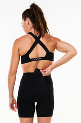 Model placing a phone in the back pocket of women's black tri shorts. Triathlon shorts with storage.